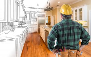 Male Contractor with Hard Hat and Tool Belt Looking At Custom Kitchen Drawing Photo Combination On White.
