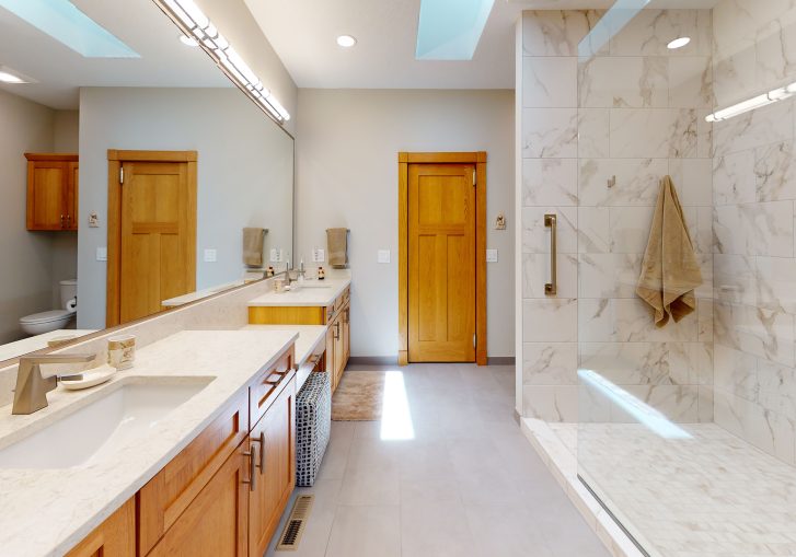 This transitional style bathroom is accented with beautiful marble backsplash, wood cabinets and bronze accents.