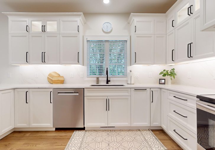 The kitchen is now a standout space, featuring Cornerstone Cabinetry in an Alabaster finish. The light cabinetry brightens the room, creating a welcoming atmosphere. A custom hood was installed, adding a striking design feature. To complete the look, the kitchen features a waterfall countertop, offering a sleek and modern touch that combines aesthetics with practicality. This kitchen is perfect for both daily use and entertaining guests.