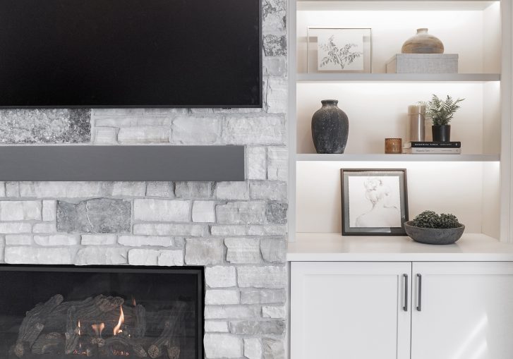 The living room remodel is a showstopper, featuring a striking stacked stone fireplace, which serves as the focal point of the space. Flanking the fireplace are custom built-in cabinets from Cornerstone Cabinetry, offering both functional storage and a polished, high-end look.