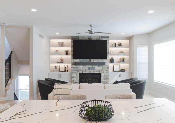 The living room remodel is a showstopper, featuring a striking stacked stone fireplace, which serves as the focal point of the space. Flanking the fireplace are custom built-in cabinets from Cornerstone Cabinetry, offering both functional storage and a polished, high-end look. The open layout enhances the flow between the kitchen, dining, and family areas, making it ideal for everyday living and entertaining.