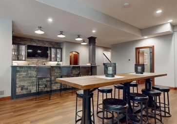 Exposed brick wall accents lend an authentic, urban speakeasy vibe. The brick's natural texture and tone create visual depth and contrast, grounding the space and connecting it to its historical inspiration.