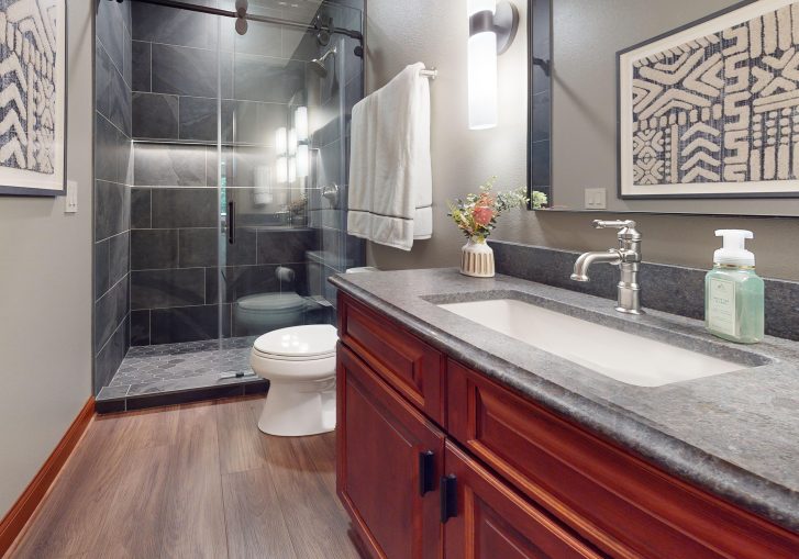 To complete the remodel, a fully finished bathroom includes modern touches like a lighted alcove in the tile shower. This space blends clean lines and spa-inspired finishes with the overall moody ambiance of the basement retreat, creating a seamless experience from bar to bath.